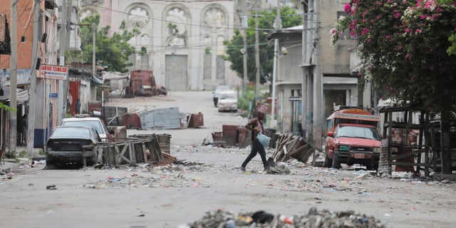 A man walks between road blocks set up by gangs after they waged intense gun battles, shuttering main avenues and a municipal market in the downtown area of the capital, in Port-au-Prince, Haiti.