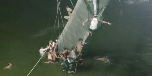 Des gens s'accrochent au pont suspendu effondré à Morbi, en Inde, le 30 octobre 2022 dans cette capture d'écran obtenue à partir d'une vidéo.  (ANI/Document via REUTERS)
