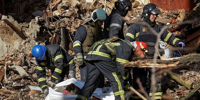 Firefighters help a local woman evacuate from a residential building destroyed by a Russian strike using an Iranian-made drone, in Kyiv, Ukraine Oct. 17, 2022.