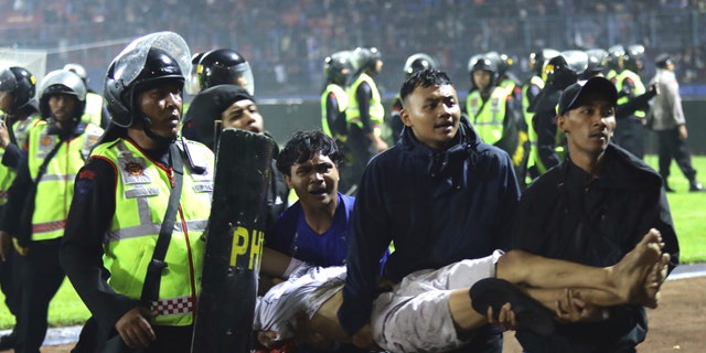 A football fan carries an injured man. More than 100 fans and dozens of police officers were killed in a clash between his two Indonesian football team supporters in East Java.