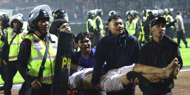 A football fan carries an injured man. More than 100 fans and dozens of police officers were killed in a clash between his two Indonesian football team supporters in East Java.