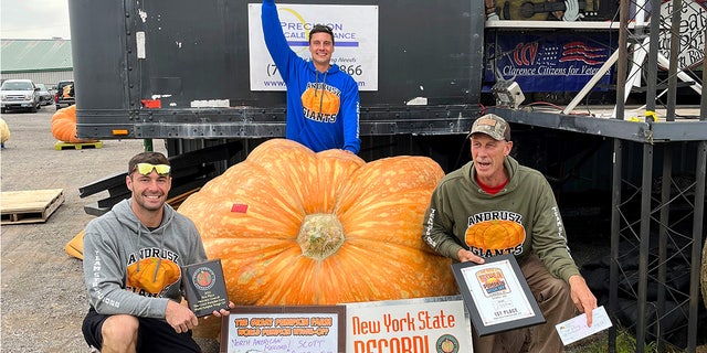 Emmett Andrusz (left), Steve Andrusz (middle) and Scott Andrusz (right), pose near their record setting 2,554-pound pumpkin at The Great Pumpkin Farm in Clarence, N.Y., on Saturday, Oct. 1, 2022.