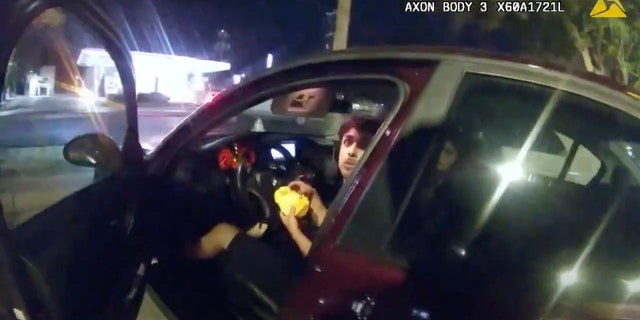 In this image taken from Oct. 2, 2022 police body camera video and released by San Antonio Police Department, Erik Cantu looks toward San Antonio Police officer James Brennand while holding a hamburger in a fast food restaurant parking lot as the officer opens the car door in San Antonio, Texas. 