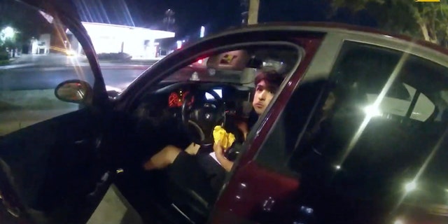 In this image taken from Oct. 2, 2022 police body camera video and released by San Antonio Police Department, Erik Cantu looks toward San Antonio Police officer James Brennand while holding a hamburger in a fast food restaurant parking lot as the officer opens the car door in San Antonio, Texas.