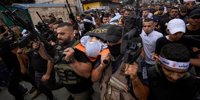 Armed Palestinians carry the body of Mahmoud Al-Sous, covered with a flag of the Islamic Jihad militant group during his funeral in the West Bank town of Jenin, Saturday, Oct. 8, 2022.