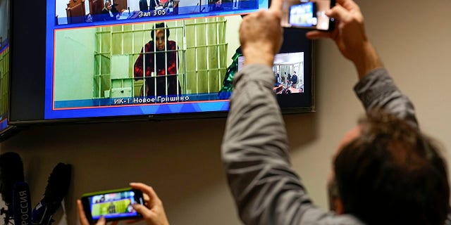 WNBA star and two-time Olympic gold medalist Brittney Griner is seen on the bottom part of a TV screen as she waits to appear in a video link provided by the Russian Federal Penitentiary Service prior to a hearing at the Moscow Regional Court in Moscow, Russia, on Oct. 25, 2022.