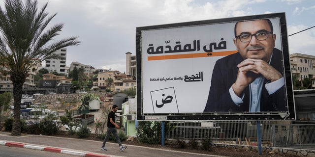 Un uomo cammina davanti a un cartellone pubblicitario della campagna elettorale che mostra Sami Abu Shehadeh, capo del partito nazionalista Balad, nella città di Umm al-Fahm, nel nord israeliano, il 21 ottobre 2022.  