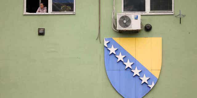 A woman looks through the window next to a flag of Bosnia and Herzegovina on Oct. 12, 2022. Bosnia-Herzegovina moved a small step closer to the European Union on Wednesday with the EU’s executive advising member states to grant it candidate member status despite criticism over how the nation is run.