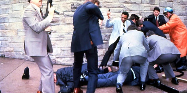 James Brady and a police officer are seen lying on the ground after being shot while the suspect John Hinckley Jr. is apprehended, at right, moments after the attempted March 30, 1981, assassination of President Ronald Reagan in Washington, D.C.