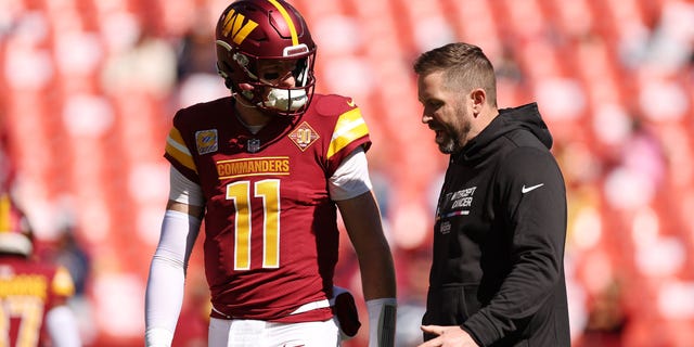 Carson Wentz #11 of the Washington Commanders talks with offensive coordinator Scott Turner before the game against the Tennessee Titans at FedExField on October 9, 2022 in Landover, Maryland.
