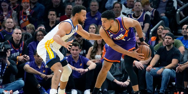 Golden State Warriors guard Stephen Curry and Phoenix Suns guard Devin Booker, #1, face off during the first half of an NBA basketball game, Tuesday, Oct. 25, 2022, in Phoenix. 