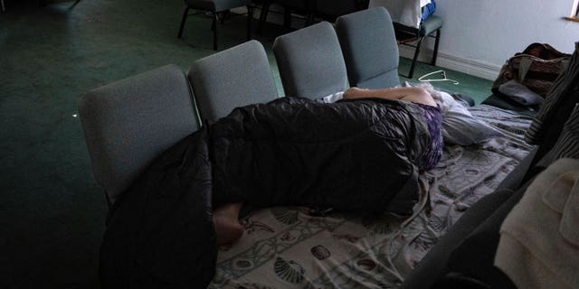 A woman sleeps on a bed of chairs inside the sanctuary of the Southwest Baptist Church in Fort Myers, Fla., on Sunday, Oct. 2, 2022. Nearly a dozen parishioners are living inside the church after their homes were destroyed by Hurricane Ian. (AP Photo/Robert Bumsted)