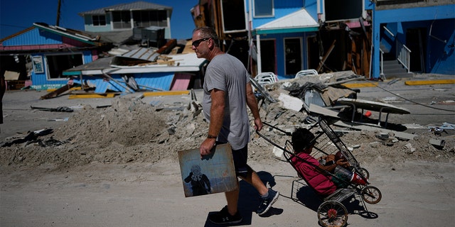 John Quigley carries a piece of artwork made by his daughter, the only thing he found to salvage from his collapsed home, as he pulls his girlfriend's son Sebastian in a cart while walking off the island, two days after the passage of Hurricane Ian, in Fort Myers Beach, Florida.