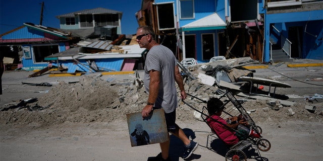 John Quigley carries a piece of artwork made by his daughter, the only thing he found to salvage from his collapsed home, as he pulls his girlfriend's son Sebastian in a cart while walking off the island, two days after the passage of Hurricane Ian, in Fort Myers Beach, Florida.