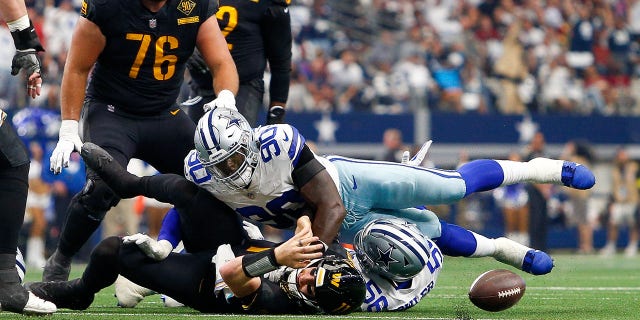 Washington Commanders quarterback Carson Wentz (11) fumbles while being sacked by Dallas Cowboys defensive ends Dante Fowler (56) and DeMarcus Lawrence (90) Oct. 2, 2022, in Arlington, Texas.