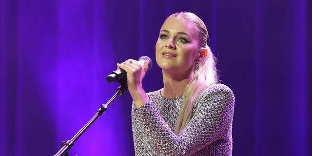Kelsea Ballerini holds a microphone on a stand at the NSAI 2022 Nashville Songwriter Awards