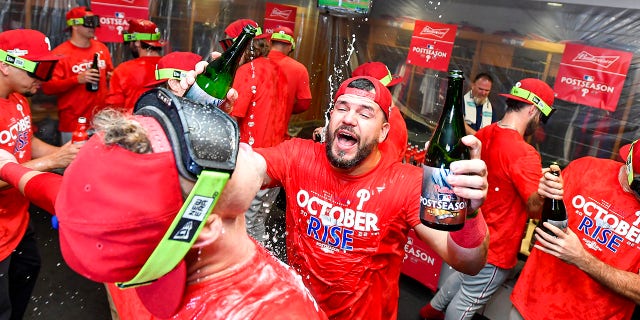 Kyle Schwarber, #12 of the Philadelphia Phillies, celebrates with teammates in the locker room after clinching the Wild Card, their first playoff berth since 2011 with a 3-0 win over the Houston Astros at Minute Maid Park on Oct. 3, 2022 in Houston.