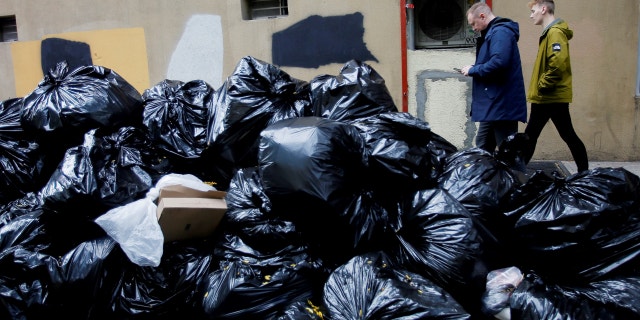 People make their way past trash bags on Oct. 18, 2022 in New York City. In an effort to deter rats and keep the area from seeming too dirty, New Yorkers will have to wait until 8 p.m. to dump their trash out.