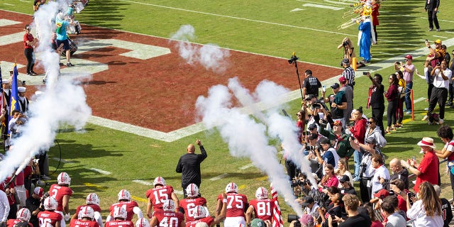 Head Coach David Shaw, wearing black, of the Stanford Cardinal leads his team onto the field before an NCAA Pac-12 college football game against the Arizona State Sun Devils on Oct. 22, 2022 at Stanford Stadium in Palo Alto, California; visible players include Brycen Tremayne carrying the American flag.