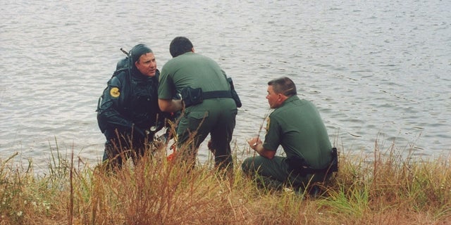 Three law enforcement officials, one clad in scuba gear, talking lakeside as they comb the water's bottom for the car of Susan Smith, who admitted to drowning her sons Michael and Alex in her car in John D. Long Lake.    