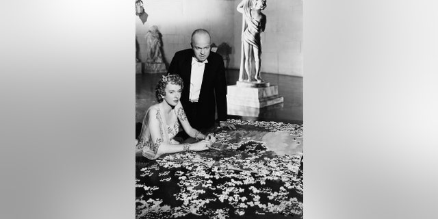 Charles Foster Kane (Orson Welles) stands over his second wife Susan Alexander Kane (Dorothy Comingore) as she puts together a puzzle in 