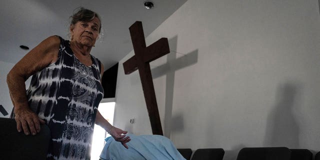 Barbara Wasko stands beside her makeshift bed on the pulpit of the Southwest Baptist Church in Fort Myers, Fla., on Sunday, Oct. 2, 2022. Wasko is living at the church after her home was destroyed by Hurricane Ian. (AP Photo/Robert Bumsted)