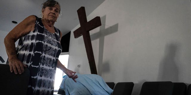 Barbara Wasko stands beside her makeshift bed on the pulpit of the Southwest Baptist Church in Fort Myers, Fla., on Sunday, Oct. 2, 2022. Wasko is living at the church after her home was destroyed by Hurricane Ian. (AP Photo/Robert Bumsted)