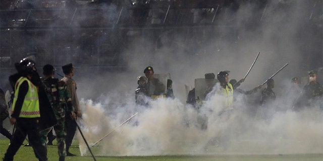 Police officers and soldiers stand amid tear gas smoke after clashes between fans during a soccer match at Kanjuruhan Stadium in Malang, East Java, Indonesia, Saturday, Oct. 1, 2022. 