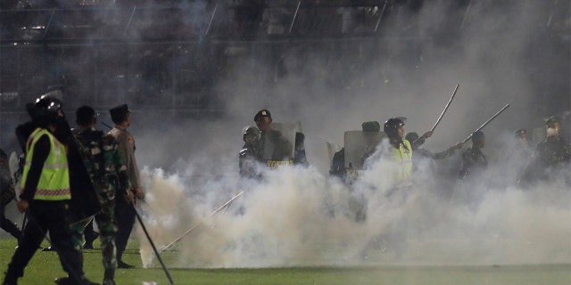 Police officers and soldiers stand amid tear gas smoke after clashes between fans during a soccer match at Kanjuruhan Stadium in Malang, East Java, Indonesia, Saturday, Oct. 1, 2022.