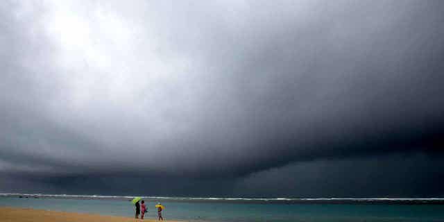 People hold umbrellas as it begins to rain on a beach in Honolulu on Dec. 6, 2021. Weather officials will release the wet season outlook for Hawaii on Oct. 19, 2022.