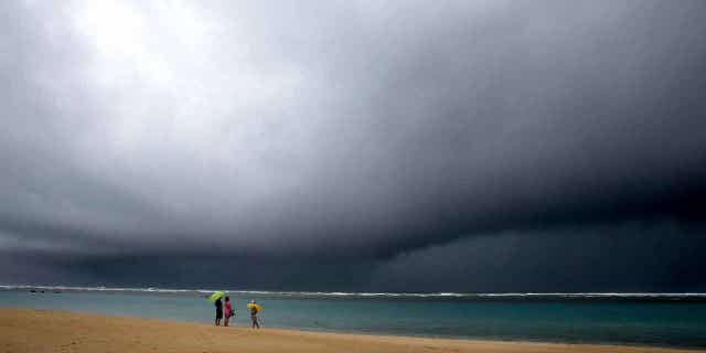 People hold umbrellas as it begins to rain on a beach in Honolulu on Dec. 6, 2021. Weather officials will release the wet season outlook for Hawaii on Oct. 19, 2022.