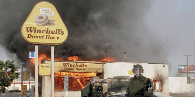 FILE - Two National guardsmen stand guard outside a burning donut shop in the aftermath of the Rodney King Verdict at Martin Luther King Boulevard and Vermont Avenue in Los Angeles, April 30, 1992. (AP Photo/Mark Elias, File)