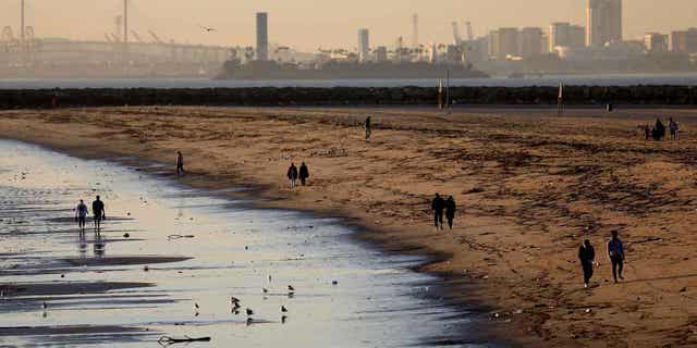 People walk along the beach on Jan. 4, 2022, in Seal Beach, CA. Sewage discharge near a creek that flows into the ocean has led to the closure of a stretch of beaches in Los Angeles.