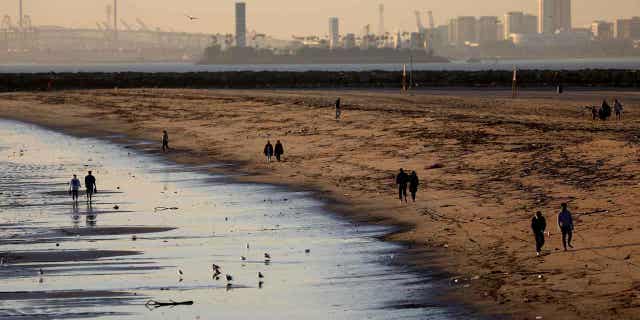 People walk along the beach on Jan. 4, 2022, in Seal Beach, CA. Sewage discharge near a creek that flows into the ocean has led to the closure of a stretch of beaches in Los Angeles.