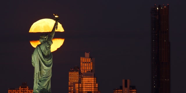 The full Hunter's Moon rises behind the skyline of Brooklyn, the Statue of Liberty and the Brooklyn Tower as the sun sets in New York City on October 9, 2022, as seen from Jersey City, New Jersey. 