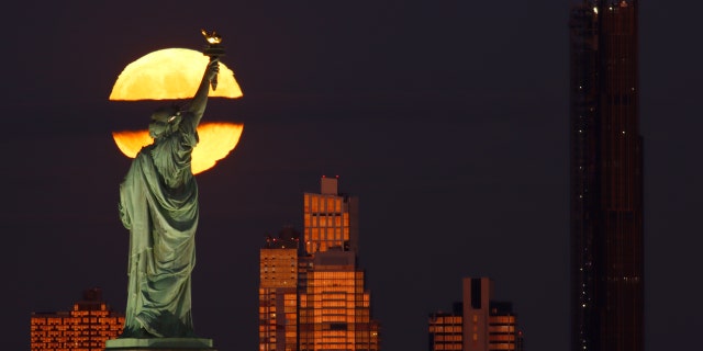 Bulan penuh Hunter terbit di balik kaki langit Brooklyn, Patung Liberty, dan Menara Brooklyn saat matahari terbenam di New York City pada 9 Oktober 2022, dilihat dari Jersey City, New Jersey.