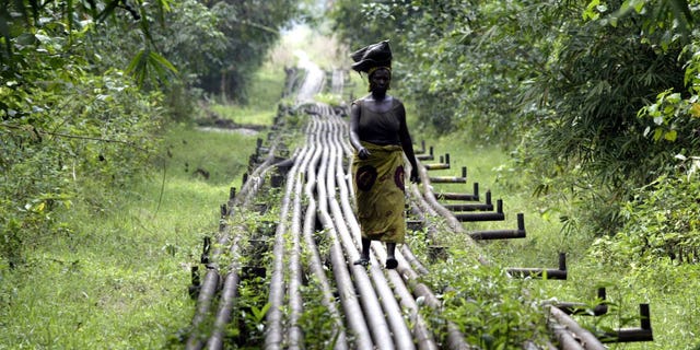 FILE- A woman walks along an oil pipeline in Warri, Nigeria, on Jan. 15, 2006. Nigerian state gas company has declared a force majeure after floods hindered gas operations, raising concerns among analysts about the West African nation's capacity to meet local and international demands. (AP Photo/George Osodi, File)
