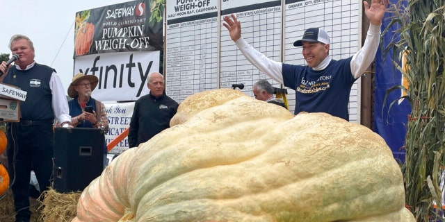 Travis Gienger from Anoka, Minnesota, stands behind his winning pumpkin at the 49th World Championship Pumpkin Weigh-Off in Half Moon Bay, California, Monday, Oct. 10, 2022.