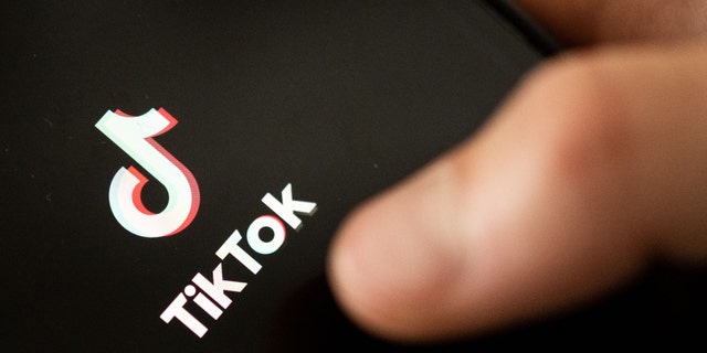 A teenager taps the TikTok logo on a smartphone.