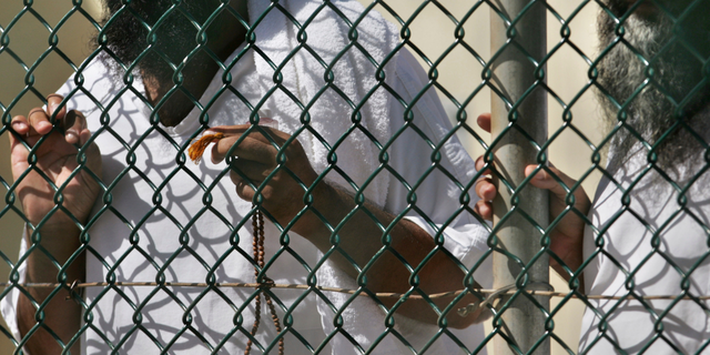 In this photo, reviewed by a US Department of Defense official, detainees stand together at a fence, one holding Islamic prayer beads, at Camp Delta prison, at the Guantanamo Bay U.S. Naval Base, Cuba.