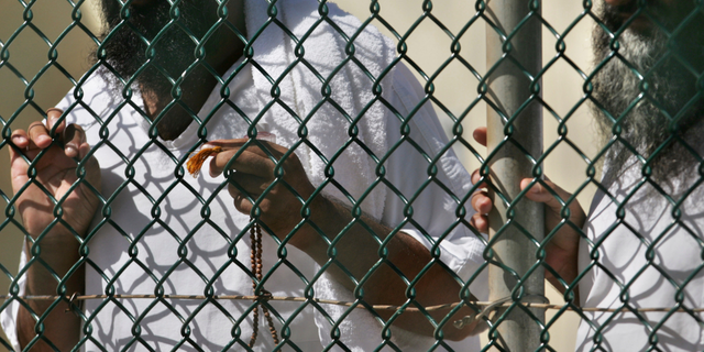 In this photo, reviewed by a US Department of Defense official, detainees stand together at a fence, one holding Islamic prayer beads, at Camp Delta prison, at the Guantanamo Bay U.S. Naval Base, Cuba.