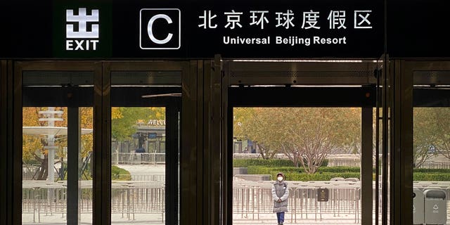 A worker wearing a face mask stands outside an exit from a subway station to stop visitors from going to the Universal Studios Beijing resort, which according to a notice was closed for epidemic control, in Beijing, Wednesday, Oct. 26, 2022. The Chinese city of Shanghai started administering an inhalable COVID-19 vaccine on Wednesday in what appears to be a world first. (AP Photo/Mark Schiefelbein)