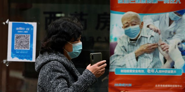 A woman wearing a face mask walks by a poster promoting the COVID-19 vaccination at a community health center in Beijing, Wednesday, Oct. 26, 2022. The Chinese city of Shanghai started administering an inhalable COVID-19 vaccine on Wednesday in what appears to be a world first. (AP Photo/Andy Wong)