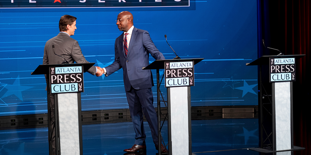 Libertarian challenger Chase Oliver, left, and U.S. Sen. Raphael Warnock, D-Ga., shake hands following the Atlanta Press Club Loudermilk-Young Debate Series in Atlanta, for the U.S. Senate race, Sunday, Oct. 16, 2022. The empty podium at right was for Republican challenger Herschel Walker, who was invited but did not attend.