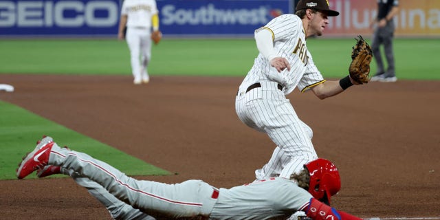 Wil Myers of the San Diego Padres, standing, scores first base before Bryson Stott of the Philadelphia Phillies slips in the fifth inning of Game 1 of the National League Championship Series at PETCO Park on October 18, 2022 in San Diego.