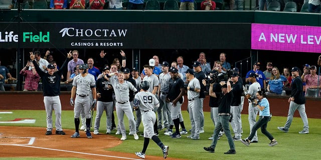 The New York Yankees' Aaron Judge (99) approaches home plate as teammates emerge to congratulate him after he hits a solo home run, his 62nd of the season, in the first inning of the second game of a doubleheader against the Texas Rangers in Arlington, Texas, Tuesday, Oct. 4, 2022.