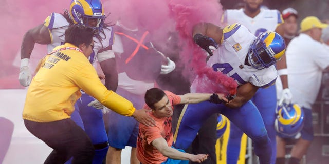 A fan with a smoke bomb is tackled on the field by Los Angeles Rams' Bobby Wagner, #45, Takkarist McKinley, #50, and a security guard during their NFL game against the San Francisco 49ers at Levi's Stadium in Santa Clara, Calif., on Monday, Oct. 3, 2022.