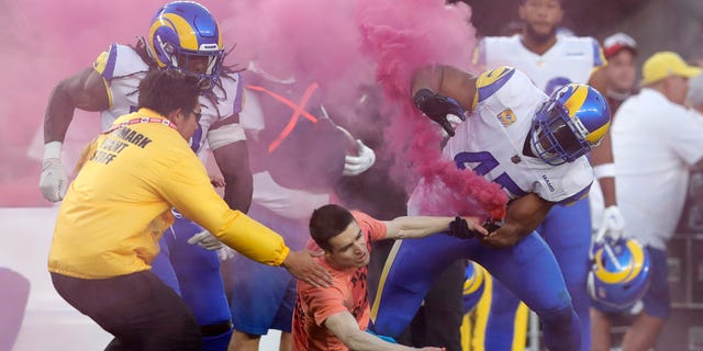 A man with a smoke bomb is tackled on the field by Los Angeles Rams' Bobby Wagner, right, Takkarist McKinley and a security guard during the game against the San Francisco 49ers at Levi's Stadium in Santa Clara, California, on Monday.