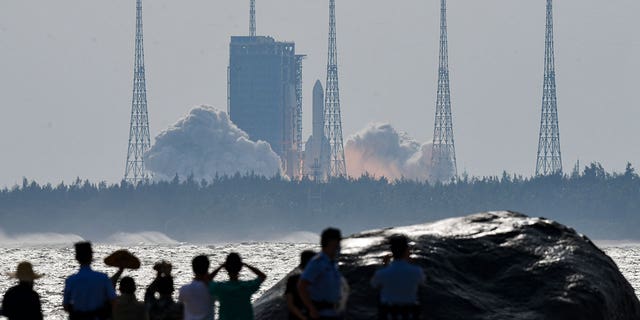 In this photo released by Xinhua News Agency, people watch the Long March-5B Y4 carrier rocket carrying the space lab module Mengtian, blasts off from the Wenchang Satellite Launch Center in south China's Hainan Province, Monday, Oct. 31, 2022.