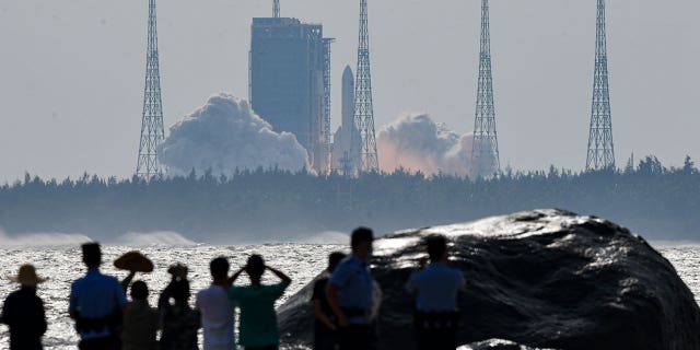 In this photo released by Xinhua News Agency, people watch the Long March-5B Y4 carrier rocket carrying the space lab module Mengtian, blasts off from the Wenchang Satellite Launch Center in south China's Hainan Province, Monday, Oct. 31, 2022.